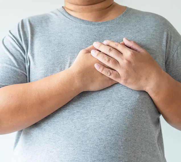 Close up image of a man from the neck to the waist in a gray t-shirt, with both of his hands on his heart