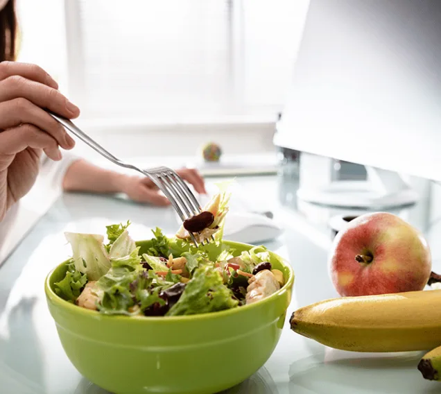 image of a person working at a desk with a salad and fruit next to their computer