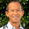 Headshot of Jeffrey Sicat, MD, FACE, FOMA wearing a white coat with a stethoscope around his neck in front of a tree