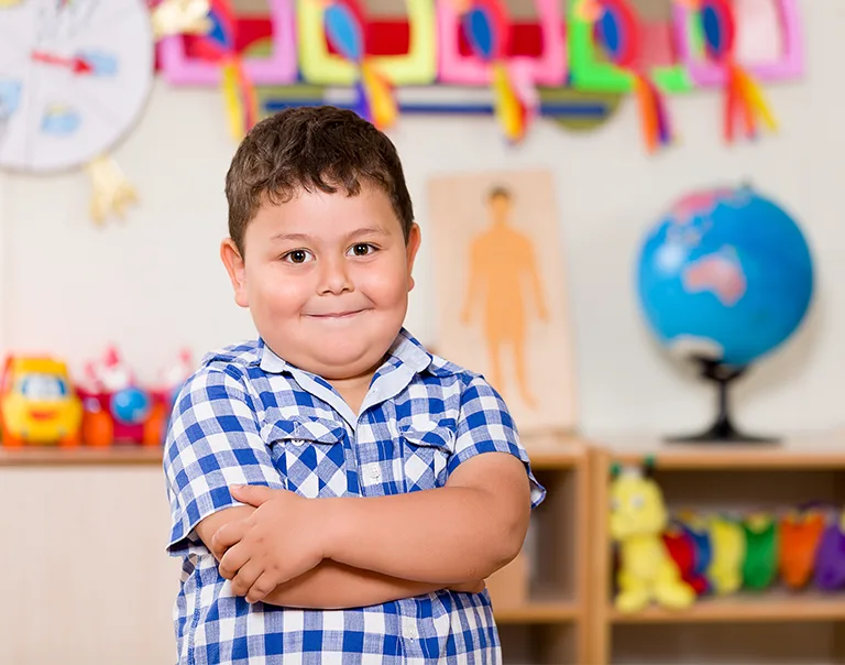 a young boy standing in a classroom with his arms crossed