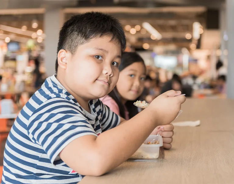 a young boy in a blue and white striped shirt sitting at a table eating