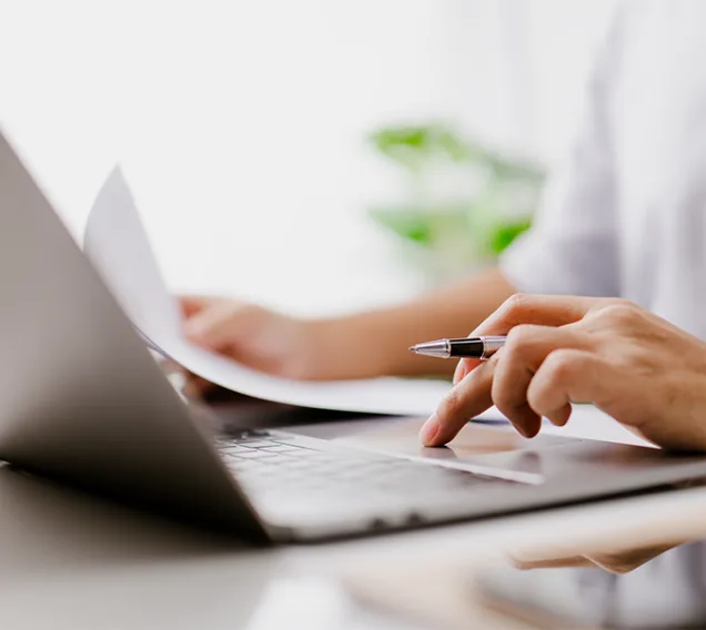 laptop with a person typing and holding a pen
