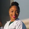 Headshot of Sylvia Gonsahn-Bollie, MD, wearing a white coat leaning up against a light post.