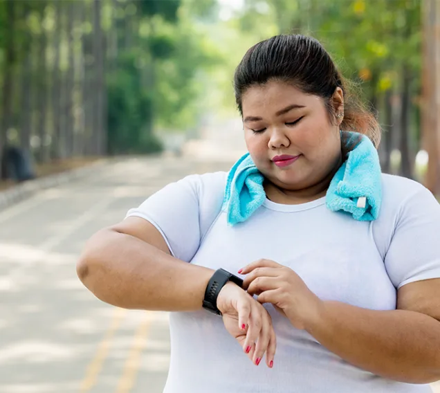 woman standing on a road with a towel around her neck, checking her watch