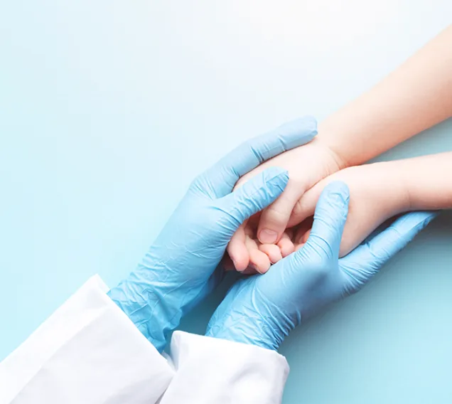 image of a doctor with blue gloves on holding a child hands