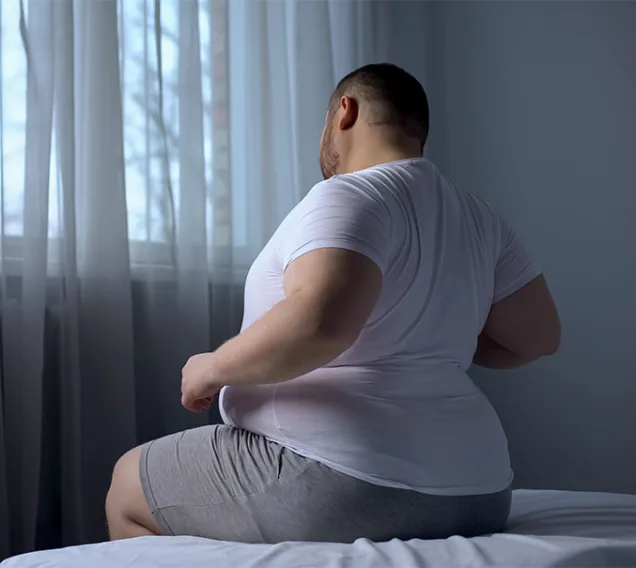 a man sitting on the edge of a bed arching his back in pain