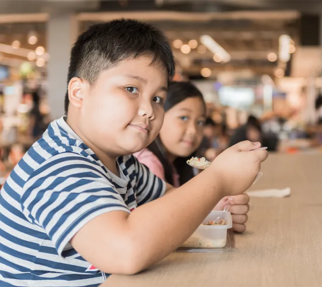 a young boy in a blue and white striped shirt sitting at a table eating
