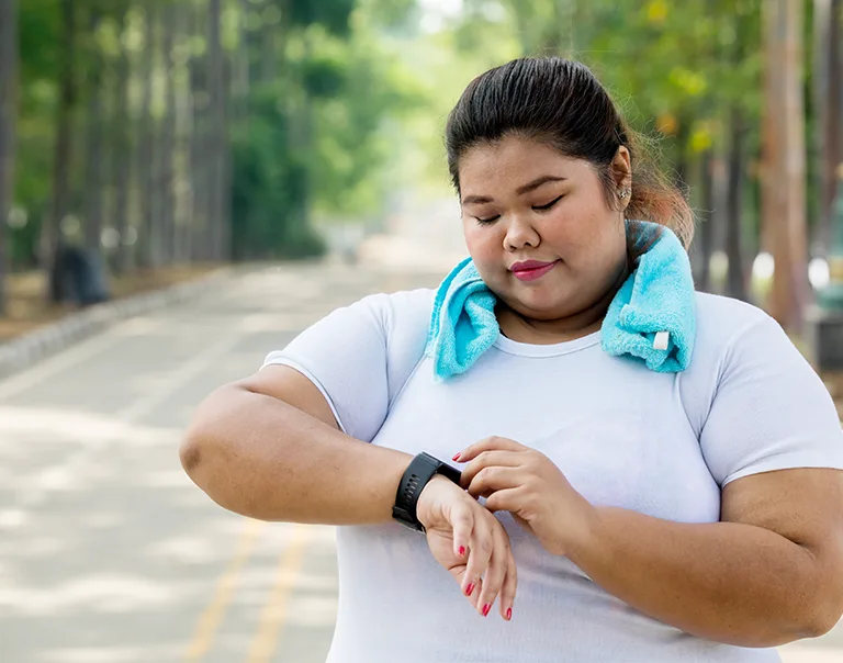 woman standing on a road with a towel around her neck, checking her watch