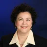 Headshot of Anna Welcome, MD, FACOG, ABOM posing in front of a blue background, wearing a black suit with yellow undershirt