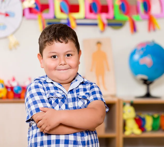 a young boy standing in a classroom with his arms crossed