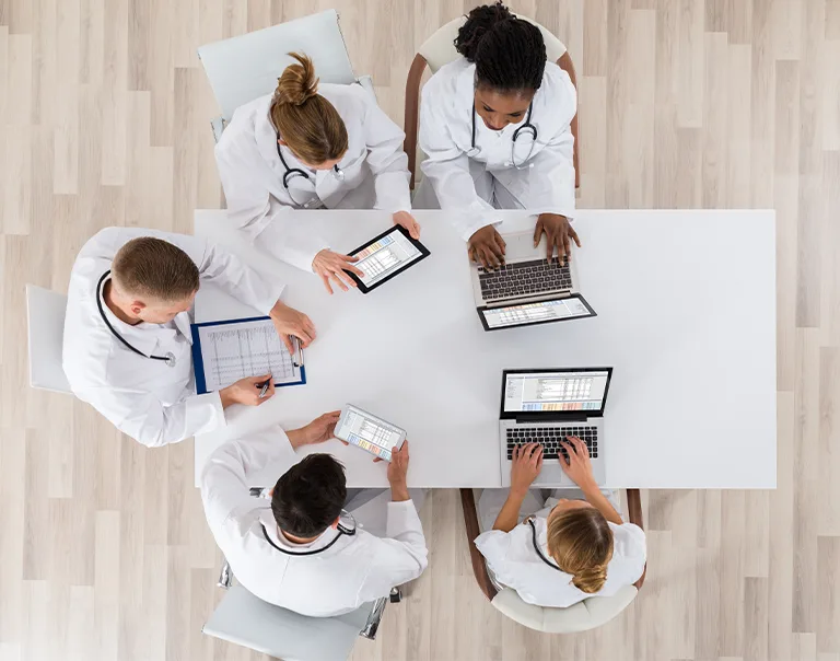 Overhead shot of doctors sitting at a table discussing with computers and laptops