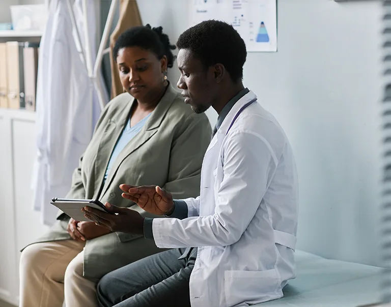 Image of a doctor sitting with a patient on a medical table, looking over paperwork with the patient