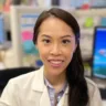 Headshot of Jennifer Ng, MD, DABOM, sitting in a white coat with a lab in the background