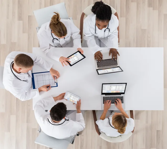 Overhead shot of doctors sitting at a table discussing with computers and laptops