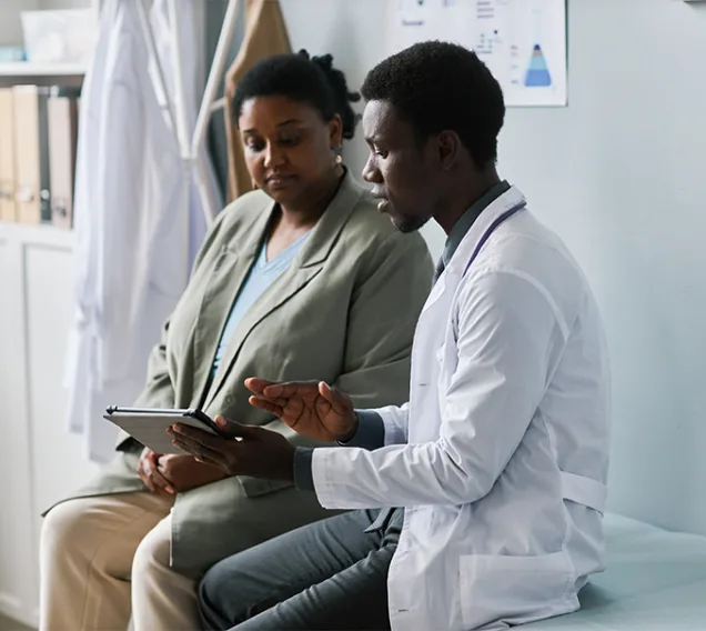 Image of a doctor sitting with a patient on a medical table, looking over paperwork with the patient