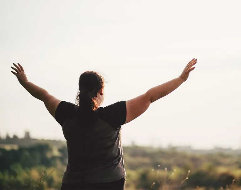 image of a woman from behind holding her arms up in front of a field