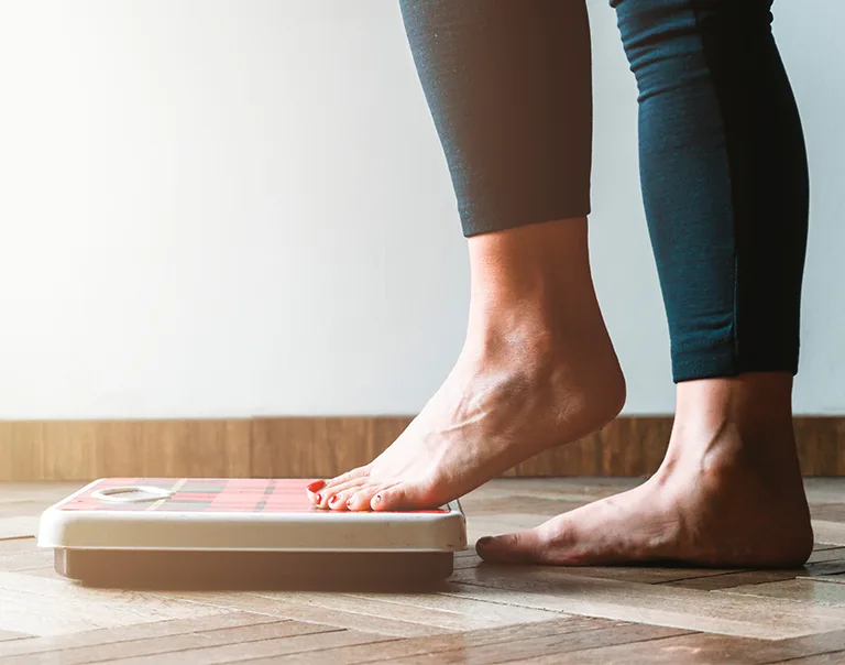 image of a scale on the floor and a woman stepping onto it
