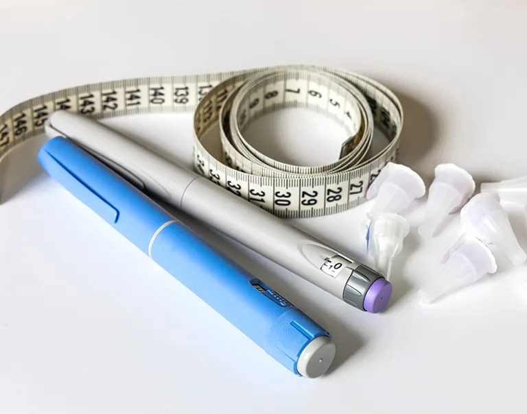 Image of 2 injectable diabetes medications with a tape measure rolled up next to it with the caps of the medications next to that