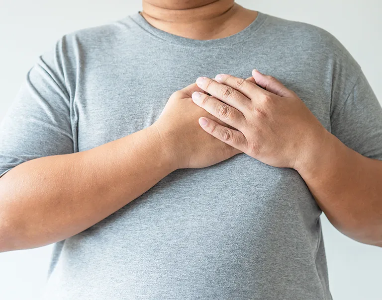 Close up image of a man from the neck to the waist in a gray t-shirt, with both of his hands on his heart