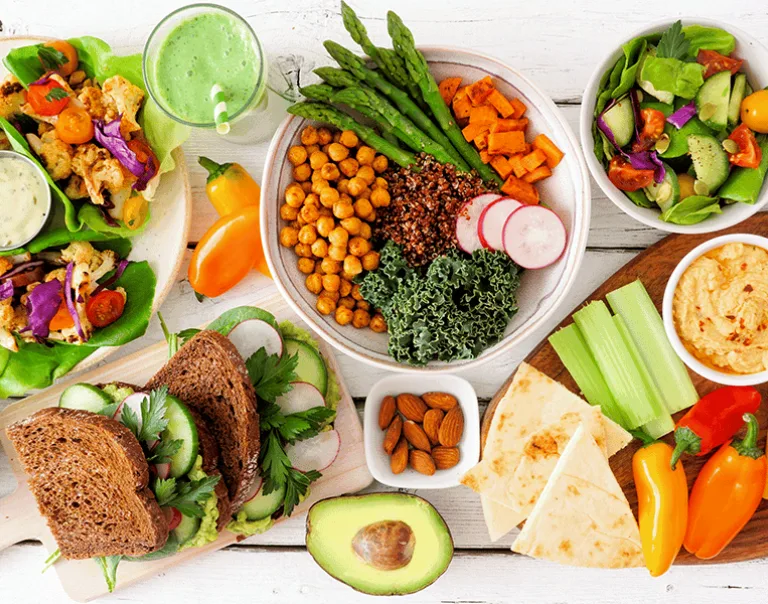 Aerial shot of a white table with a variety of bowls of fruit, vegetables, grains, and carbs