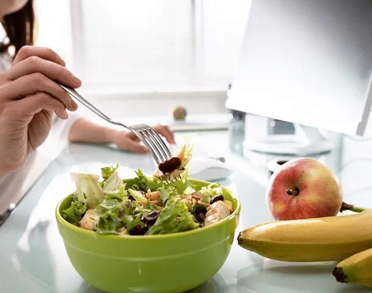 image of a person working at a desk with a salad and fruit next to their computer