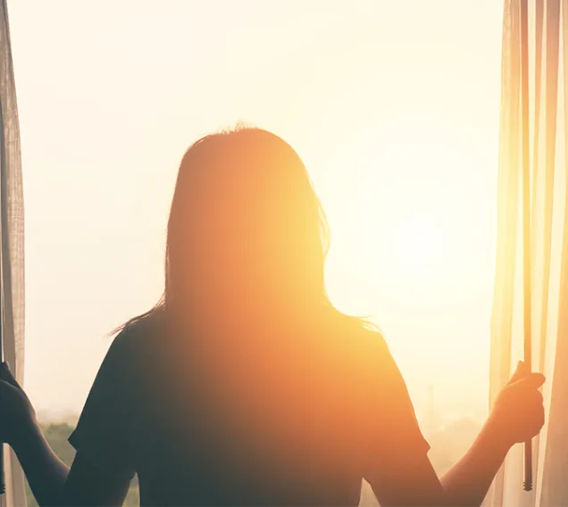 person standing in front of a window, opening the curtains to the morning sun