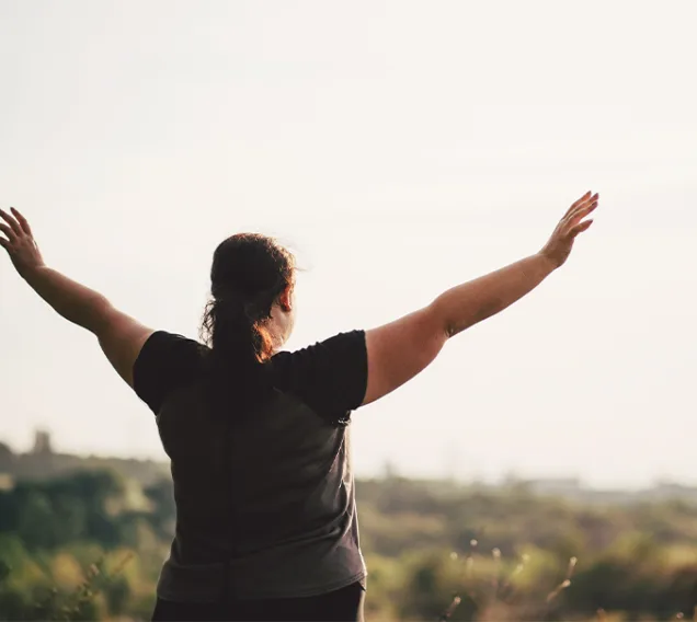 image of a woman from behind holding her arms up in front of a field