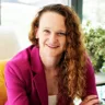 Headshot of Carolynn Francavilla Brown, MD, FOMA, DABOM sitting on a a yellow chair in a pink suit with a window and plants in the background