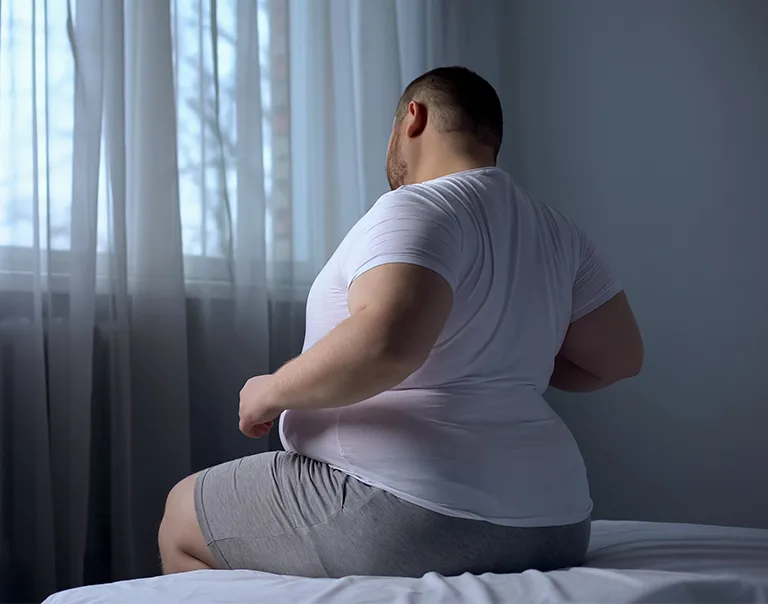 a man sitting on the edge of a bed arching his back in pain