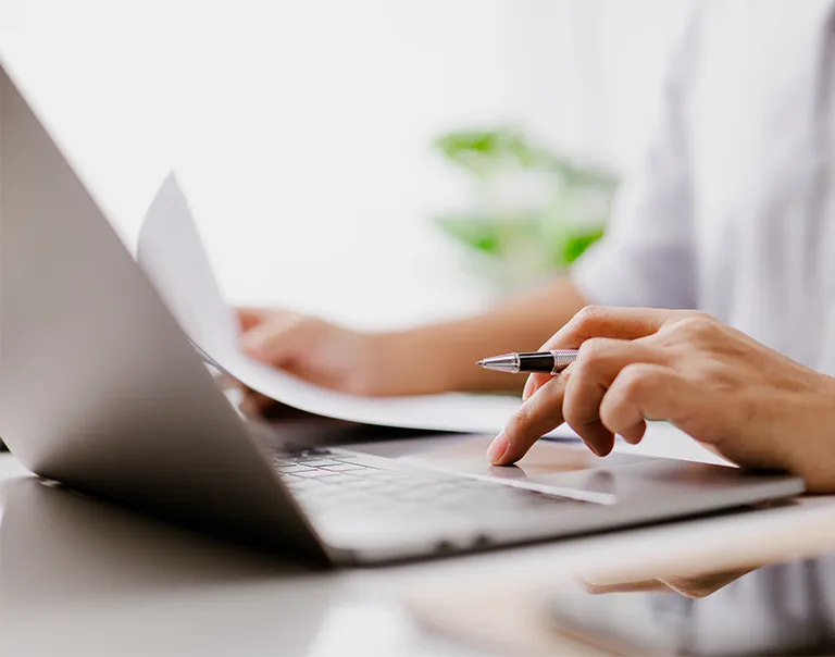 laptop with a person typing and holding a pen